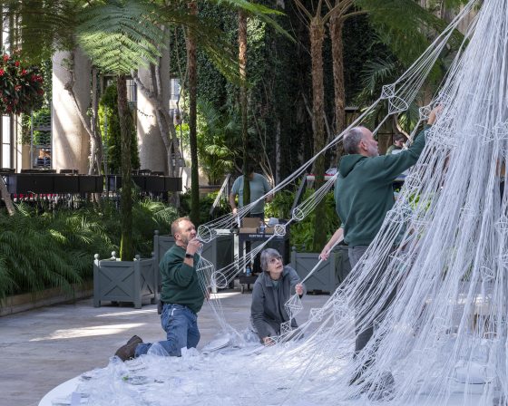 A group of people arranging white geometric forms and strings into the shape of a tree. 